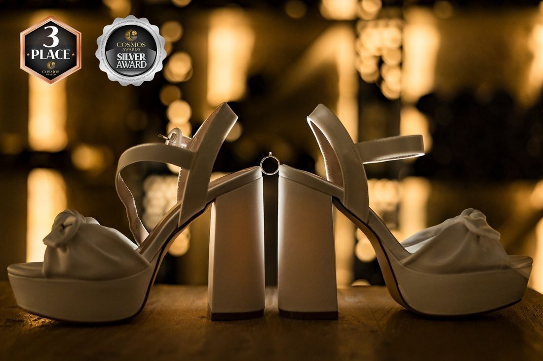 Zwei Brautschuhe mit dem Verlobungsring zwischen den Absätzen vor goldenem Bokeh